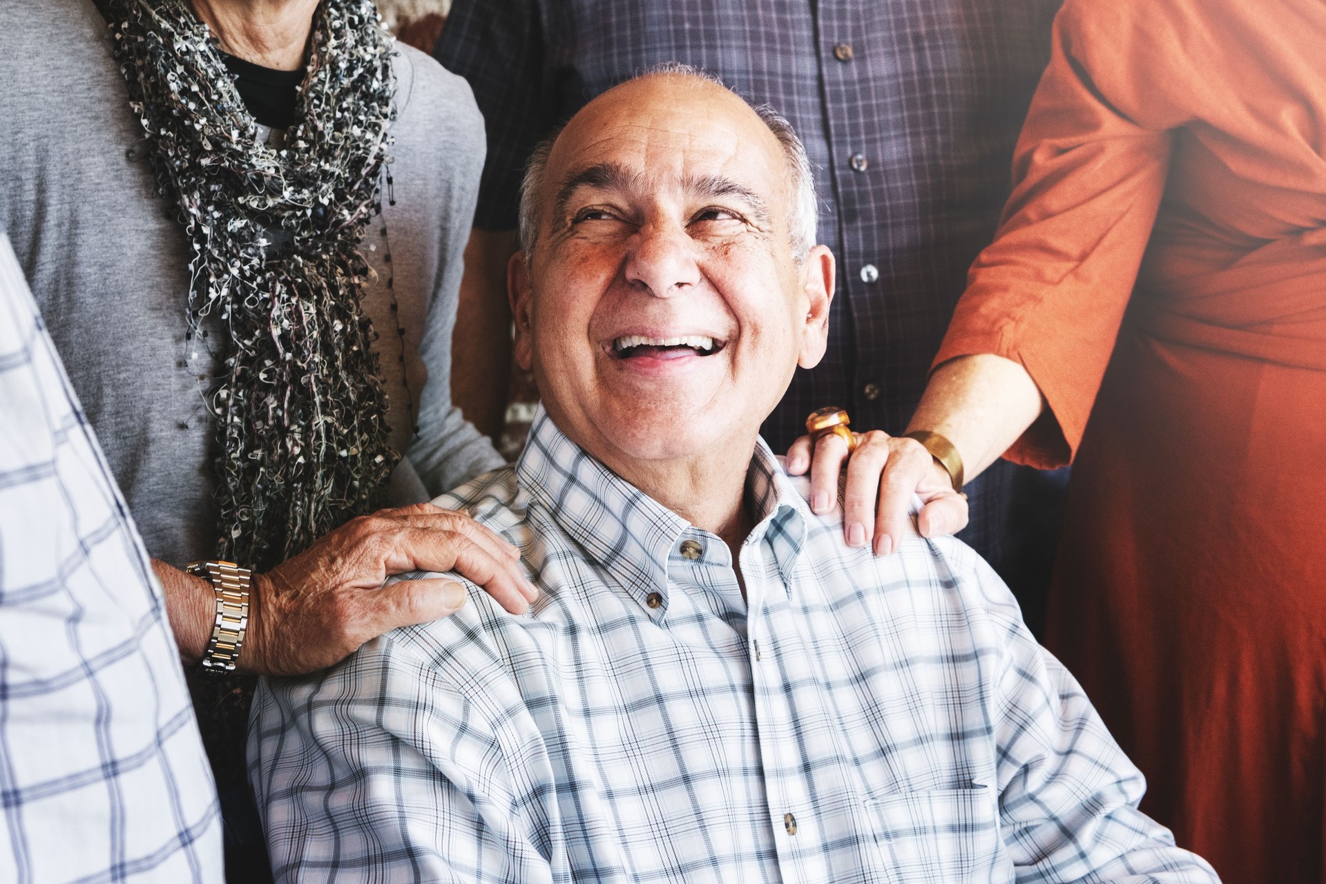 Elderly man smiling, surrounded by group of senior adults smiling and interacting.